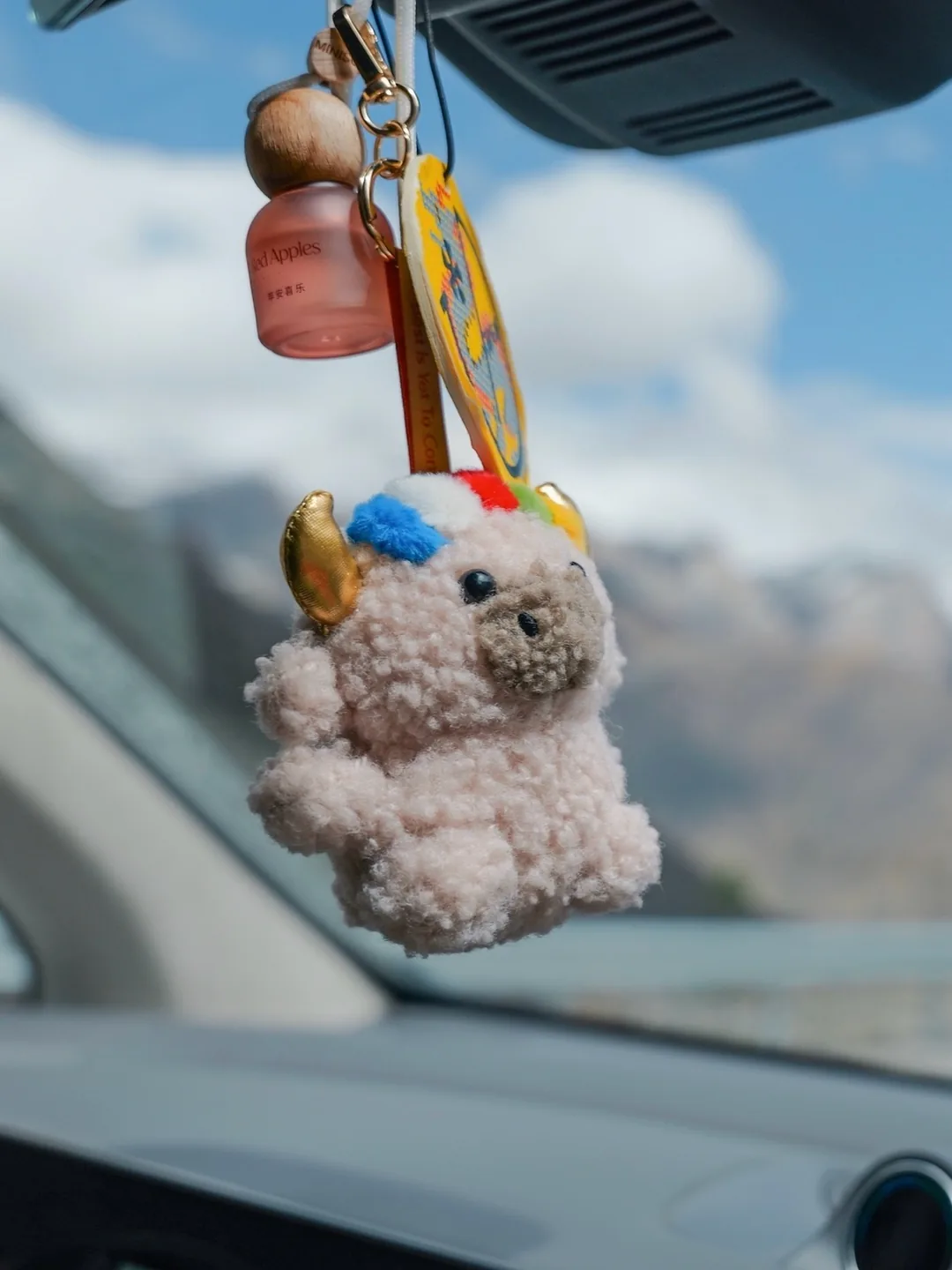 Dele hanging as a car charm from the rearview mirror, mountains visible through the windshield — 車內後視鏡上掛著的德勒車掛