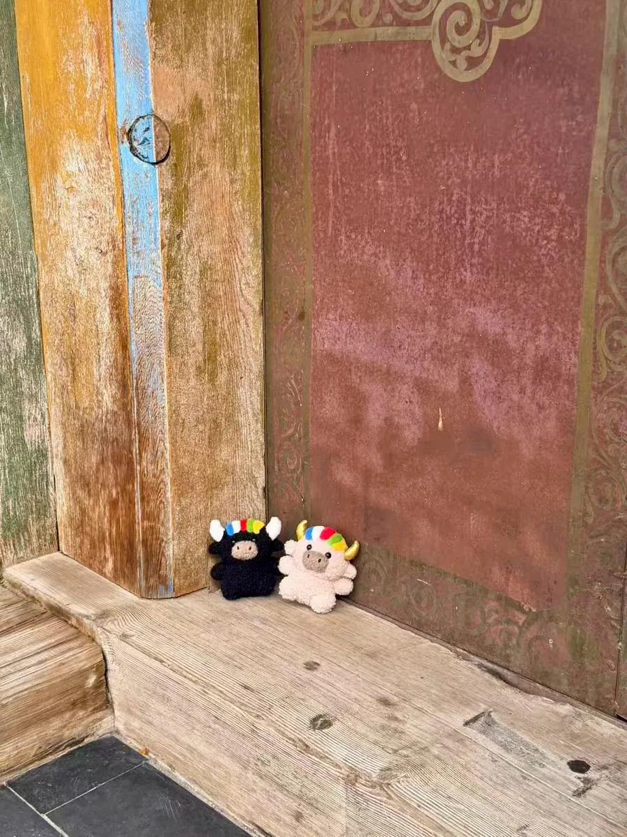 Tashi and Dele sitting together on the worn wooden threshold of an old temple door — 寺廟舊木門門檻上的扎西與德勒